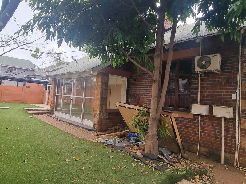 Rear view of a brick and stone house featuring a sliding glass door entrance, artificial lawn, and an external air conditioning unit.