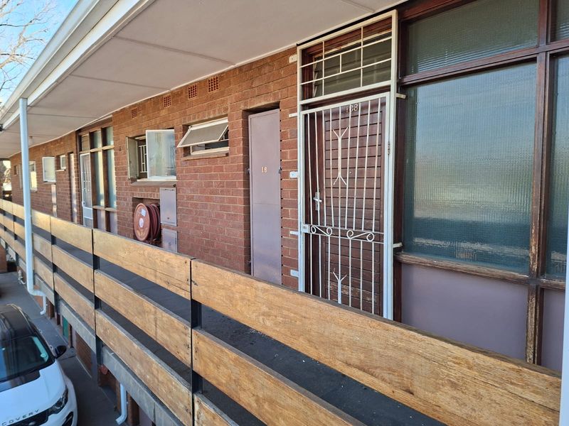 Exterior view of an apartment building walkway featuring brick facade, security gates, and a timber balustrade.