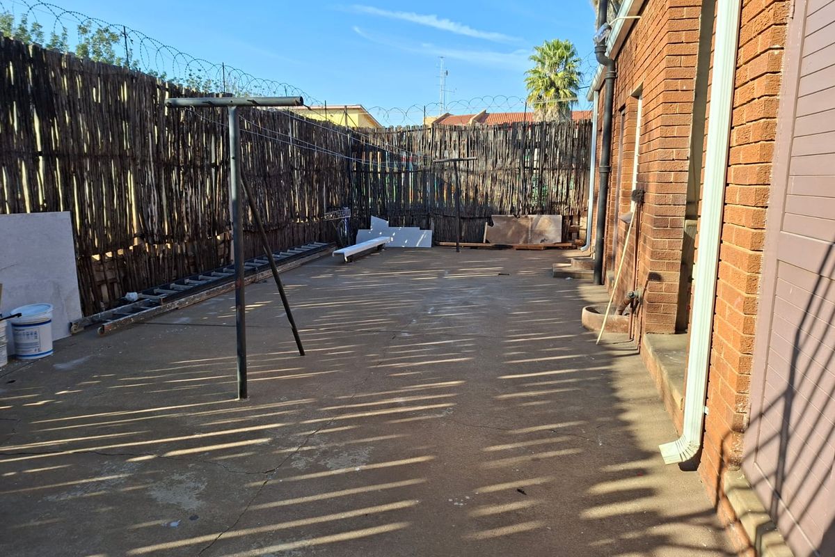 A rear exterior area featuring brick walling, concrete paving, and perimeter fencing with security wire.