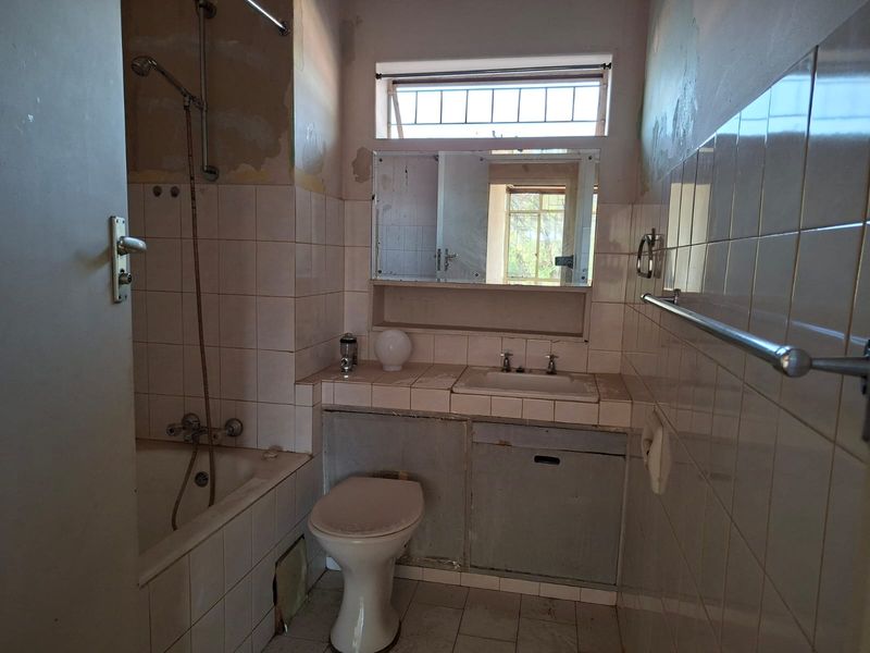 A dated bathroom featuring a built-in vanity, bathtub, and toilet, currently requiring significant renovation and cosmetic updates to restore its functionality and appeal.