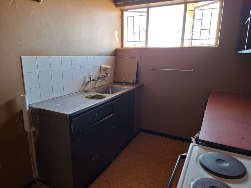 A dated kitchen area featuring a stainless steel sink, tiled splashback, and built-in cabinetry, requiring cosmetic updates and repairs to the wall finishes.