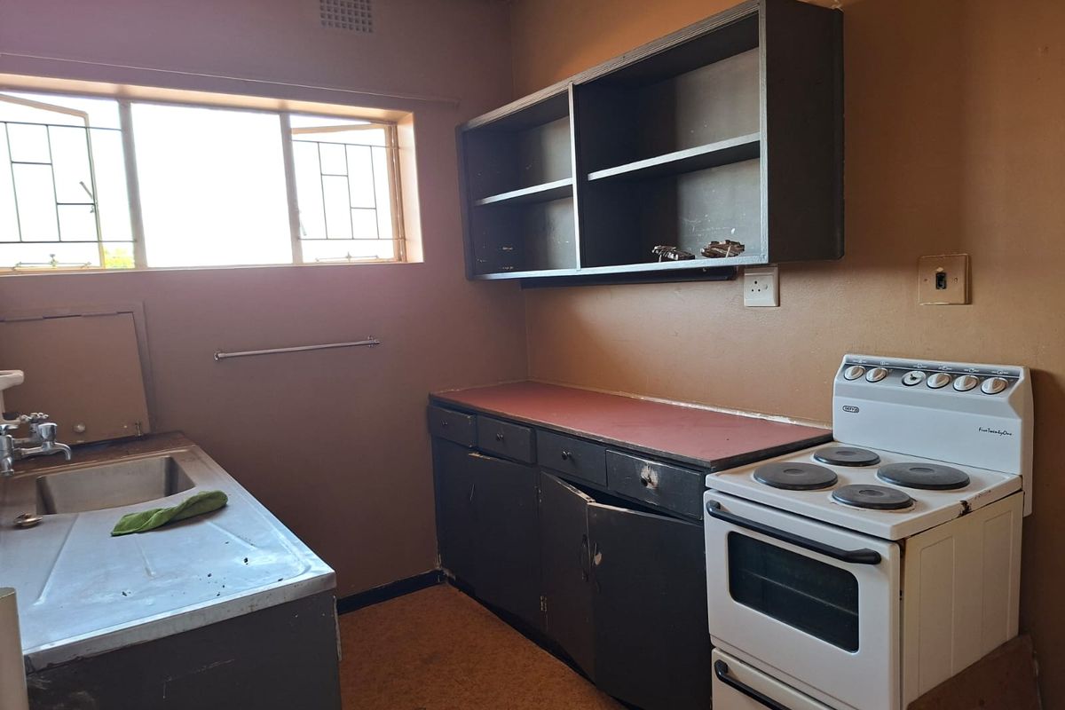 A dated kitchen featuring original cabinetry, a stainless steel sink, and a freestanding electric stove, requiring renovation to modernize the space.