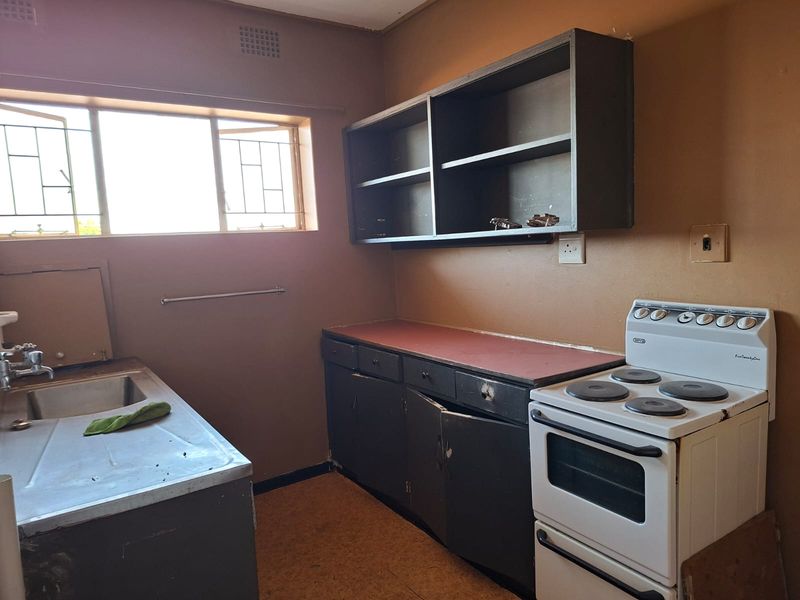 A dated kitchen featuring original cabinetry, a stainless steel sink, and a freestanding electric stove, requiring renovation to modernize the space.