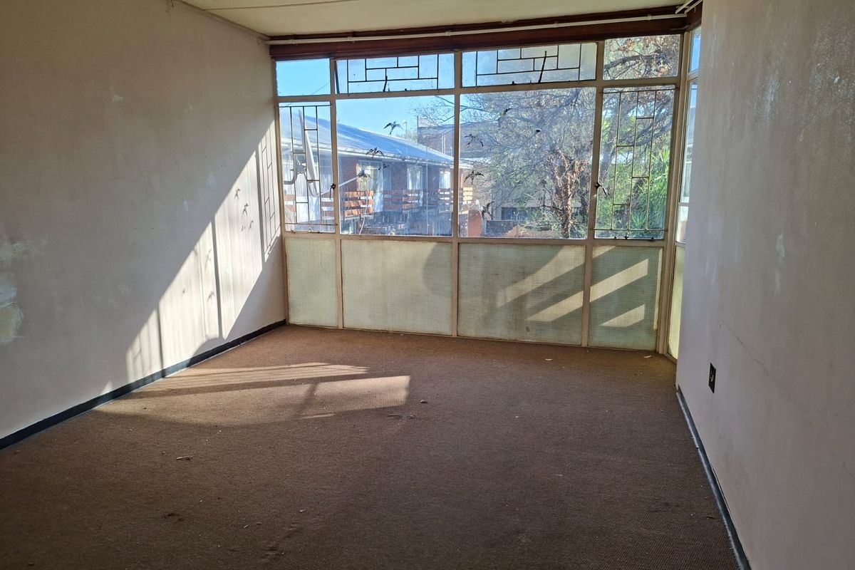 An empty living room featuring a large metal-framed window wall, requiring cosmetic updates to the walls and flooring to restore its appeal.