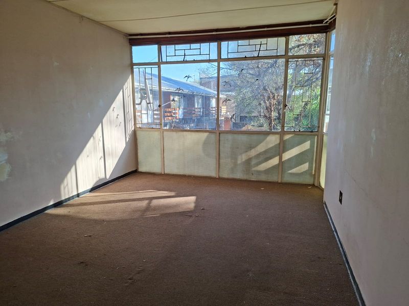 An empty living room featuring a large metal-framed window wall, requiring cosmetic updates to the walls and flooring to restore its appeal.