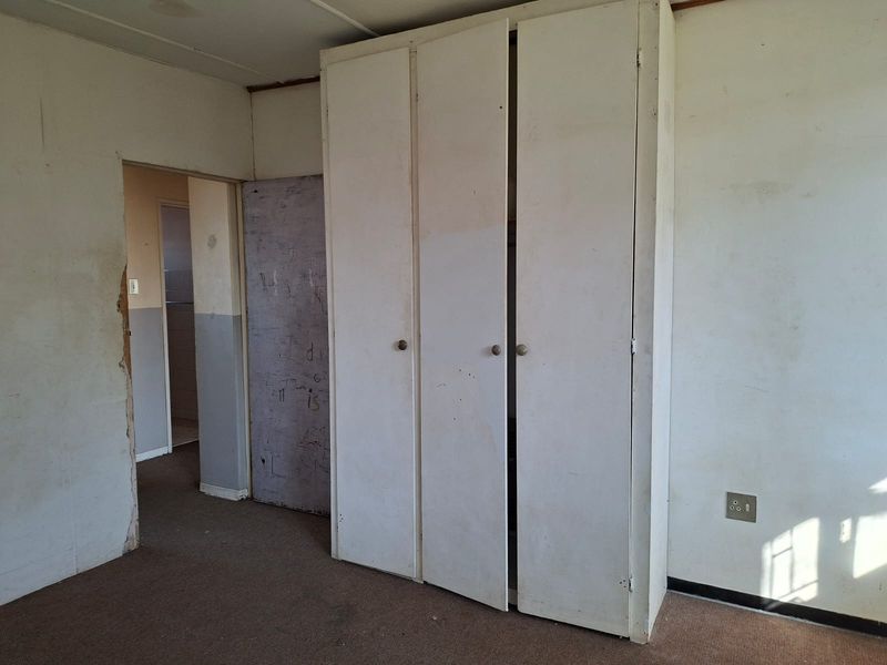 An empty bedroom featuring built-in wardrobes, carpet flooring, and visible wear on the walls and door frames, requiring cosmetic refurbishment.