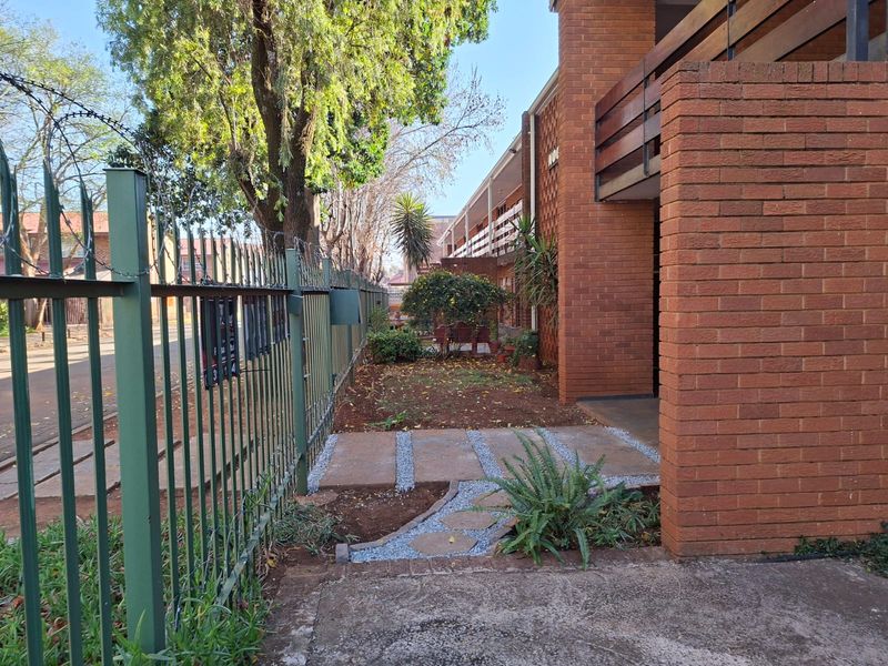 Exterior view of the apartment building facade featuring a brick structure, metal security fencing with razor wire, and a paved garden walkway.
