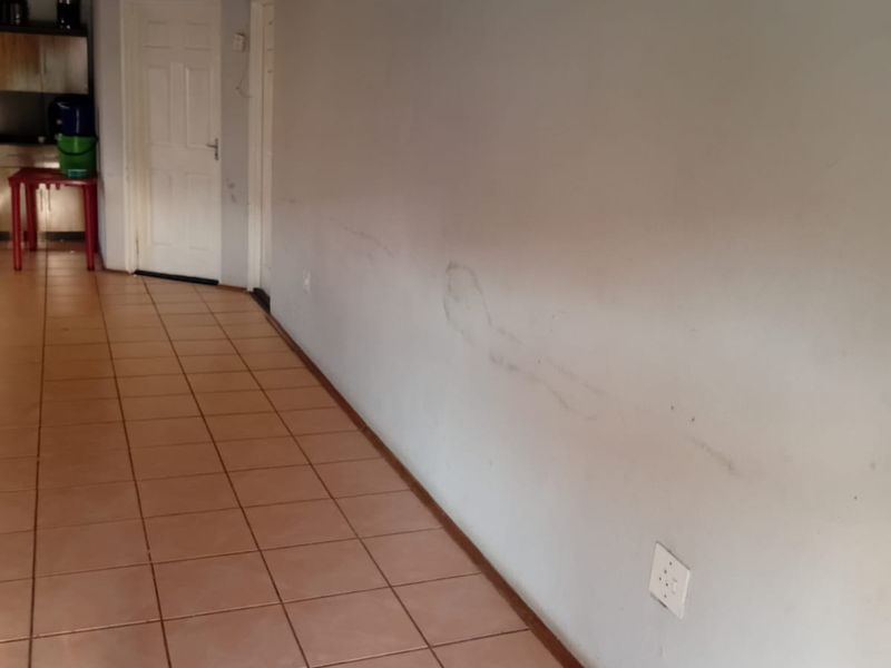 A long hallway featuring ceramic floor tiles, showing visible signs of wear and staining on the walls and ceiling.