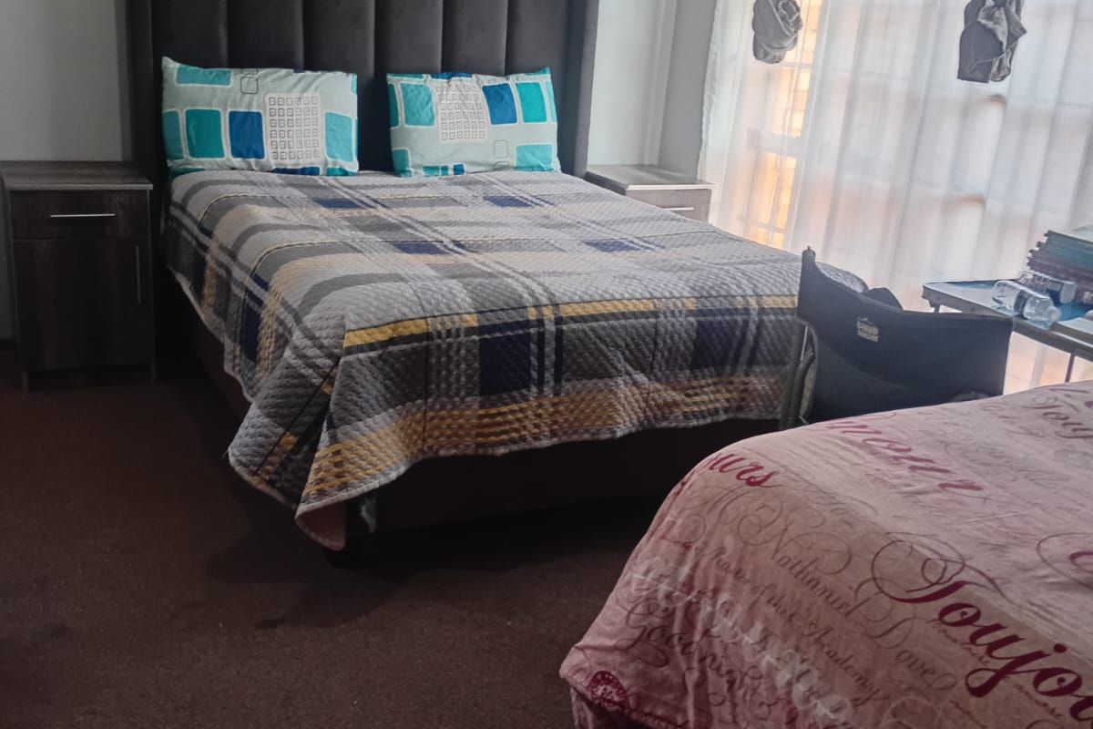 A functional bedroom featuring carpeted flooring, curtain rails, and a wall-mounted electrical distribution board.