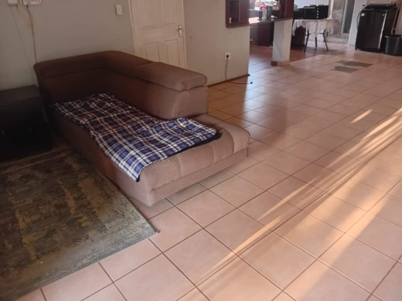 An open-plan living area featuring tiled flooring and a breakfast bar, connecting to a secondary kitchen or utility space.