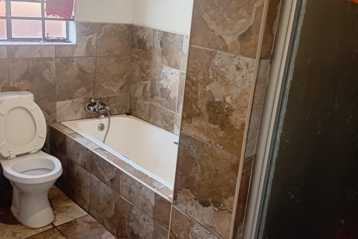A functional bathroom featuring a built-in bathtub, toilet, and shower enclosure with brown stone-look wall and floor tiling.