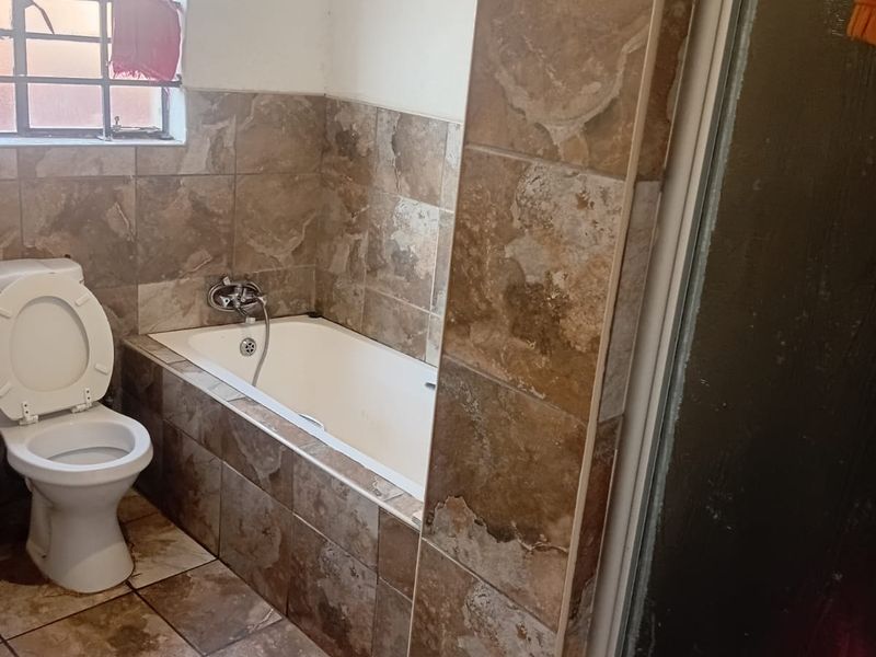 A functional bathroom featuring a built-in bathtub, toilet, and shower enclosure with brown stone-look wall and floor tiling.