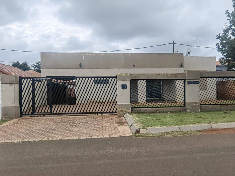 Front elevation of a residential property featuring a paved driveway, secure metal gate, and concrete boundary walling.