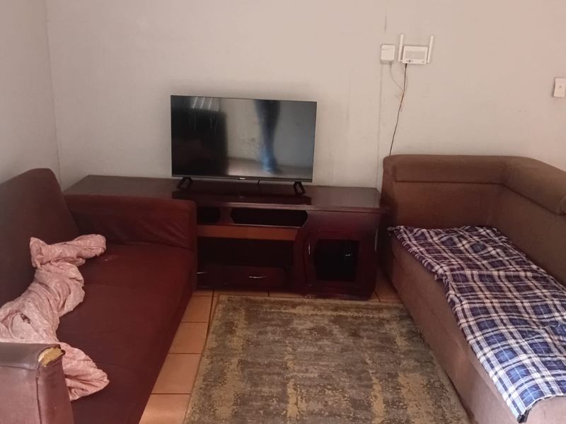 A compact living room area featuring tiled flooring and visible wall imperfections, offering a functional space ready for cosmetic updates and modernization.