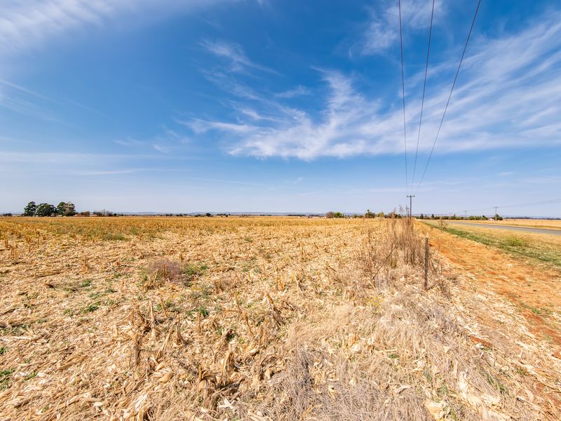 A wide-angle view of a vacant residential plot featuring dry vegetation, a wire fence boundary, and adjacent overhead power lines.