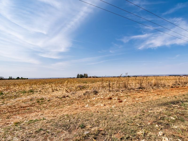 A wide, open expanse of vacant residential land featuring dry vegetation, wire fencing, and overhead power lines under a clear blue sky.
