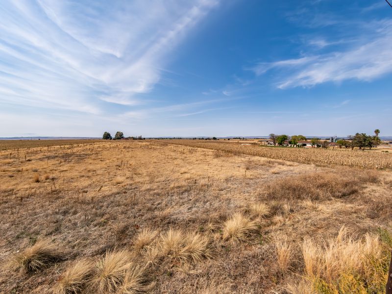 A wide-angle view of expansive, undeveloped residential land featuring dry grassland under a clear blue sky.