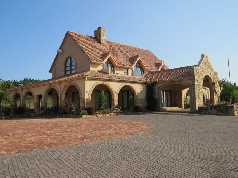 A well-maintained residential property featuring a distinctive terracotta tiled roof, stone-clad facade, and an expansive arched veranda overlooking a paved driveway.