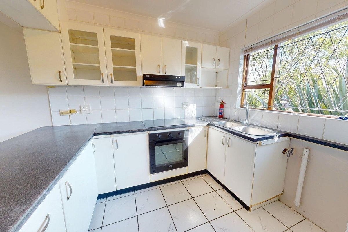 A functional kitchen featuring white cabinetry, dark laminate countertops, built-in oven and hob, tiled backsplash, and tiled flooring with natural light.