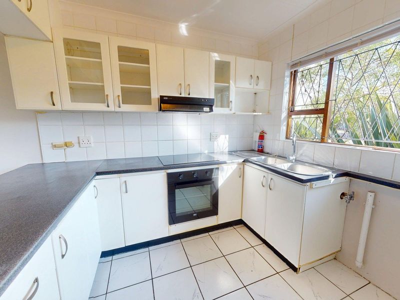 A functional kitchen featuring white cabinetry, dark laminate countertops, built-in oven and hob, tiled backsplash, and tiled flooring with natural light.