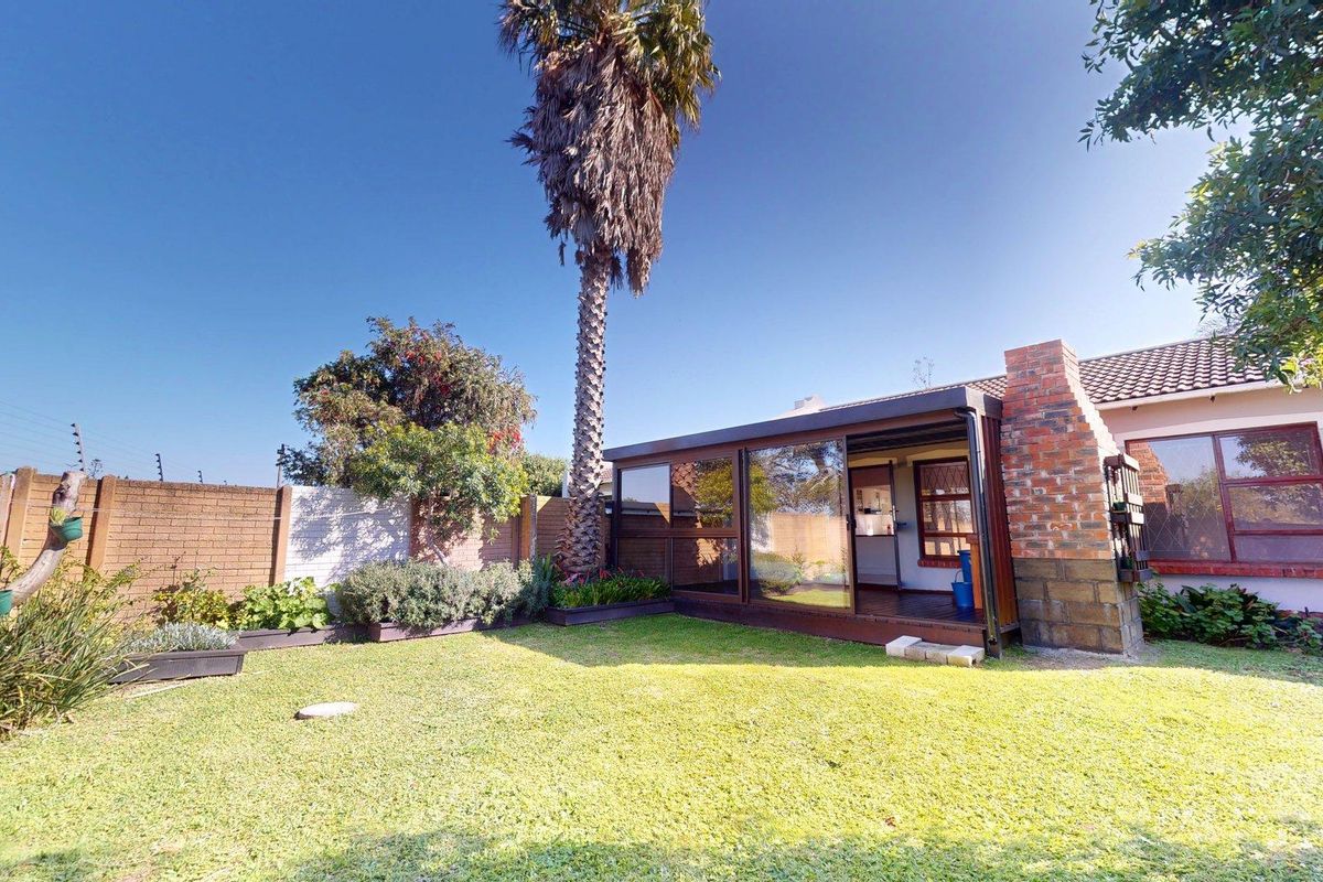 Rear garden view featuring a lawn, a brick boundary wall, and an enclosed patio area with an integrated brick fireplace.