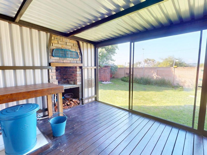 Covered patio featuring a built-in brick braai, timber decking, and sliding glass doors overlooking the rear garden.