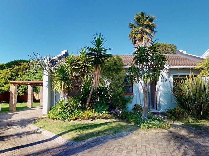 Front elevation of a townhouse featuring a paved driveway, established garden, and a covered pergola area.