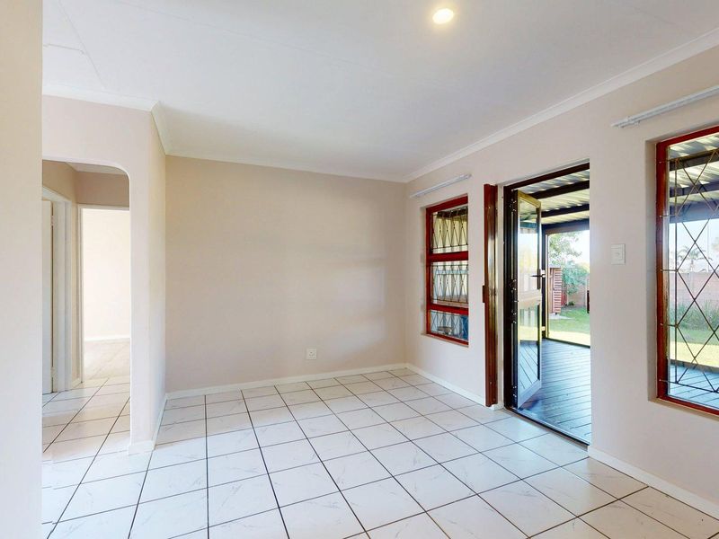 An empty living area featuring tiled flooring, security bars on windows, and direct access to an outdoor patio space.