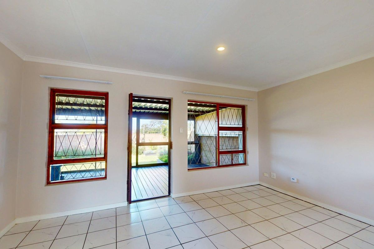 A bright, empty living room featuring tiled flooring, security bars on the windows, and direct access to an outdoor patio area.