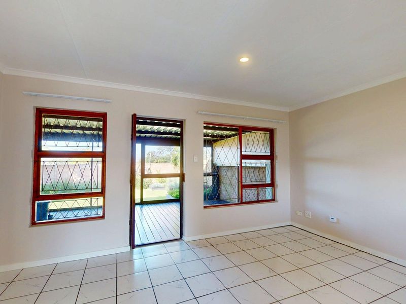 A bright, empty living room featuring tiled flooring, security bars on the windows, and direct access to an outdoor patio area.