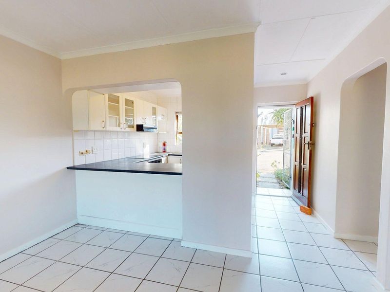 Open plan living area featuring tiled flooring, a functional kitchen with built-in cabinetry, and direct access to the front entrance.