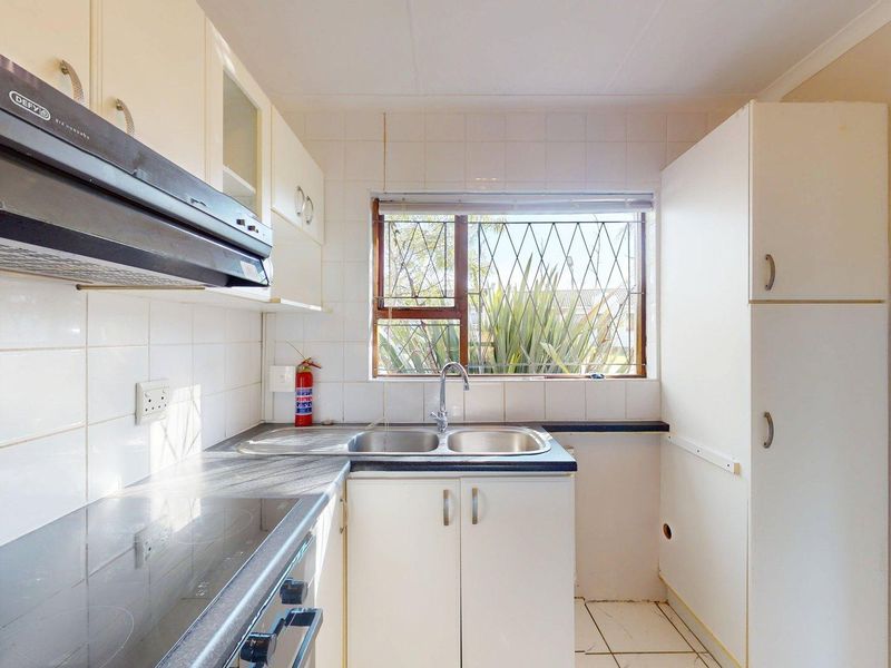 A functional kitchen featuring built-in cabinetry, a double sink, and an electric stove, with a window providing natural light and security bars.