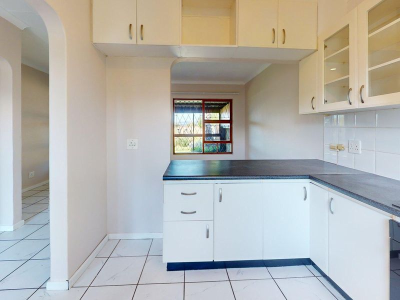 A clean, functional kitchen featuring white cabinetry, dark countertops, tiled flooring, and a built-in oven with an extractor fan.