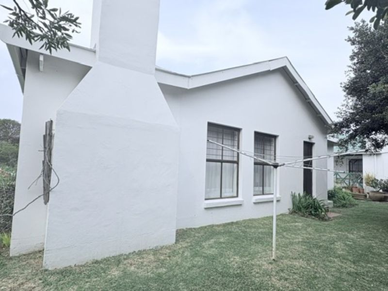 Rear exterior view of the house featuring a prominent chimney, gabled roofline, and established garden area.