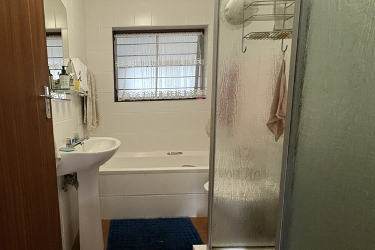 A functional bathroom featuring a pedestal basin, a built-in bathtub, and a separate shower enclosure with tiled finishes throughout.
