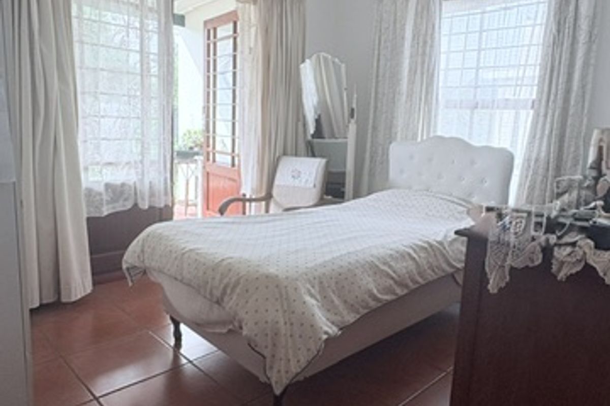 A bedroom featuring terracotta floor tiles, a ceiling light fixture, and direct access to an outdoor area through glass-paned french doors.