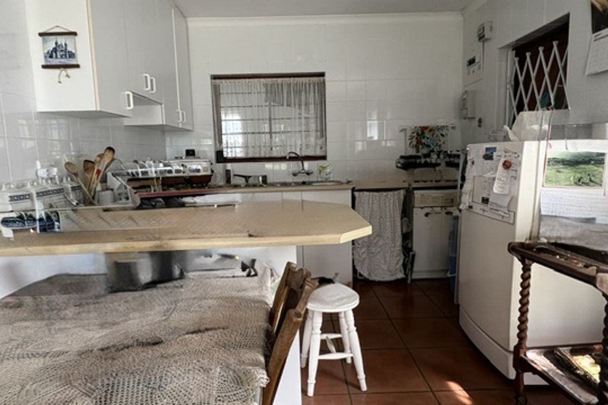 A functional kitchen featuring white built-in cabinetry, tiled splashbacks, and tiled flooring, offering a practical layout with potential for modern updates.