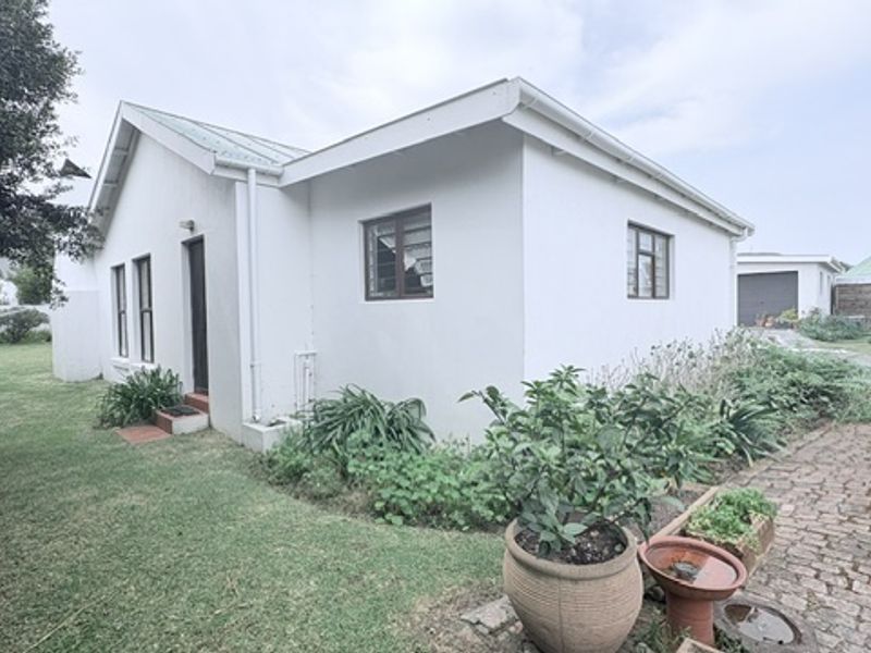 A view of the rear exterior of the house, featuring a paved driveway, lawn, and white painted facade.