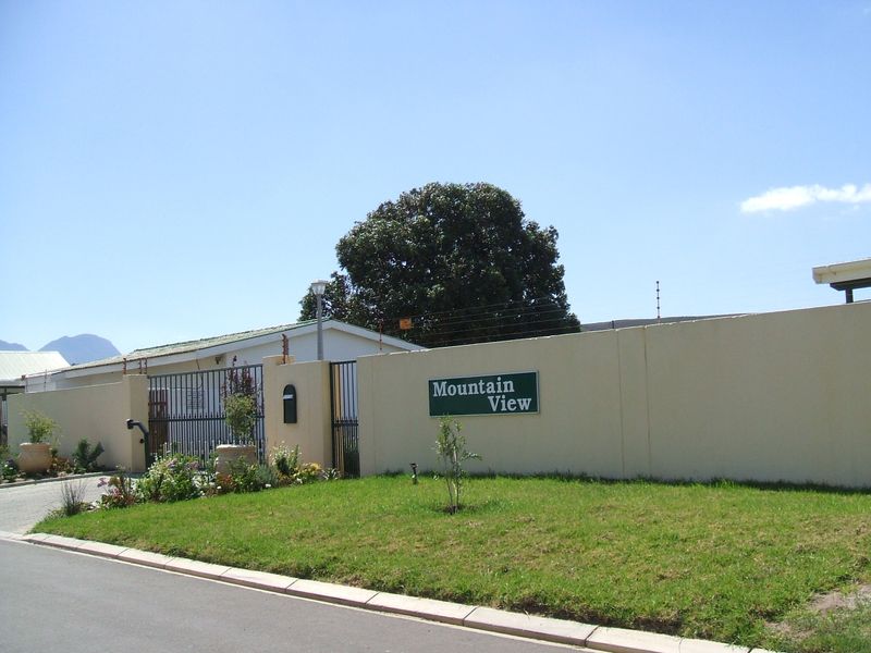 Front view of the property entrance featuring a secure perimeter wall with electric fencing, metal gate, and paved driveway access.