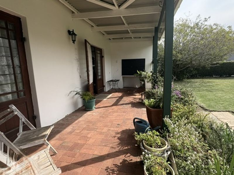 A covered patio area featuring brick paving, a built-in braai, and direct access to the garden through timber framed doors.