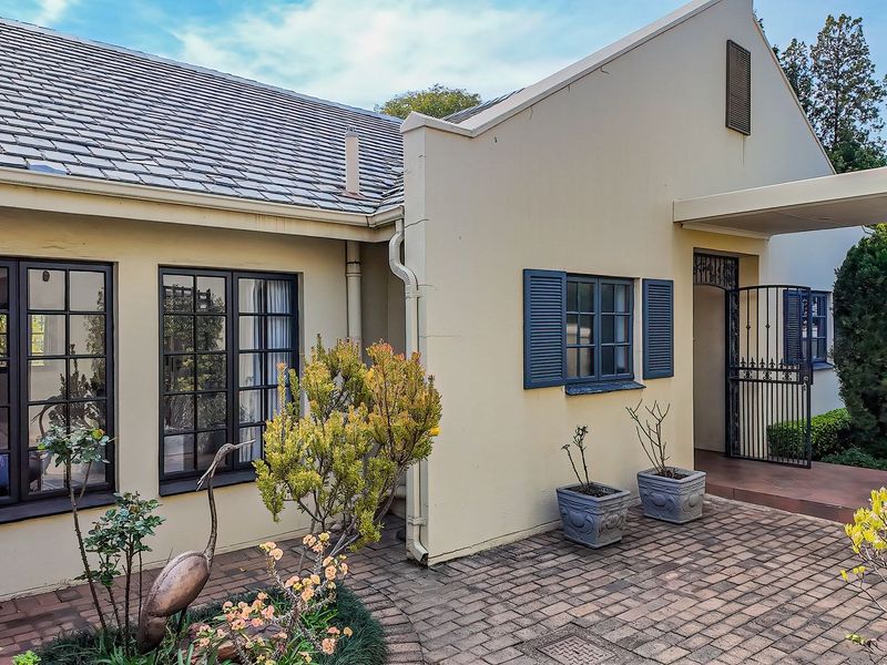 Front facade of a traditional house featuring a tiled roof, paved entrance area, and secure wrought iron gate access.