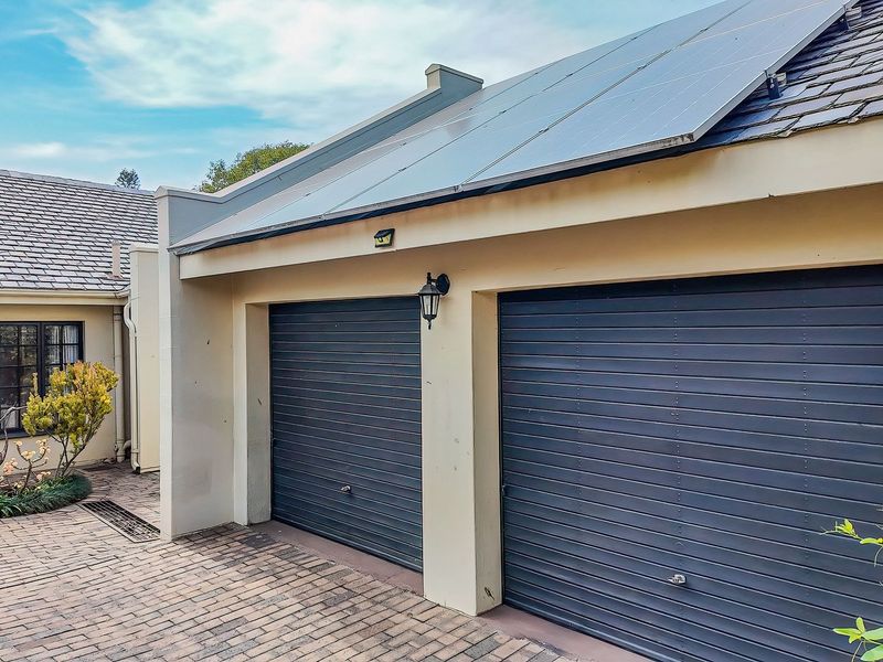A well-maintained double garage featuring dark horizontal doors, solar panels on the roof, and a neat brick-paved entrance area.