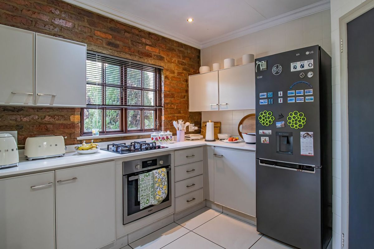 A functional kitchen featuring exposed brick walls, modern white cabinetry, a built-in oven, gas hob, and tiled flooring.