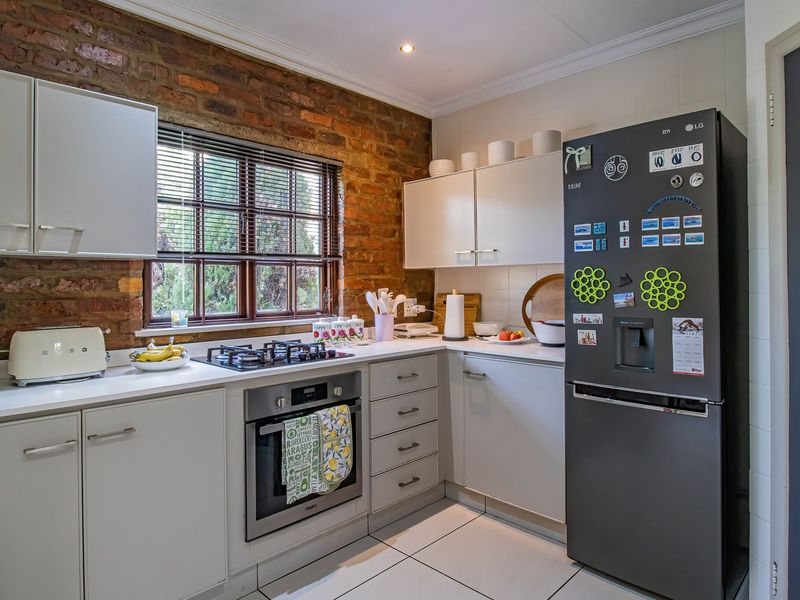 A functional kitchen featuring exposed brick walls, modern white cabinetry, a built-in oven, gas hob, and tiled flooring.