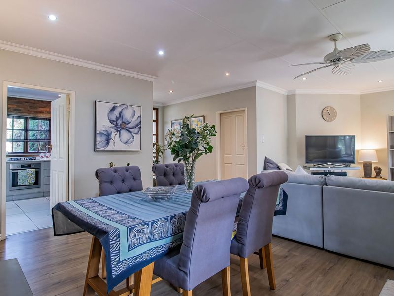 An open-plan living and dining area featuring laminate flooring, recessed downlights, and a ceiling fan, with a view into the adjacent kitchen.