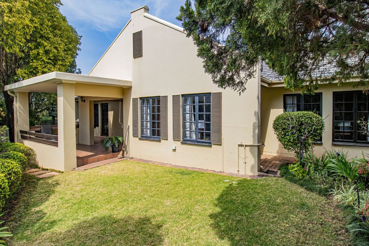 Rear view of the property featuring a covered patio, well-maintained lawn, landscaped garden, and classic casement windows with shutters.