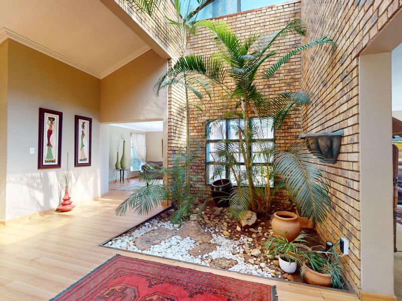 Spacious entrance hall featuring an internal garden bed, exposed brick walls, and a large skylight providing natural light to the central living area.