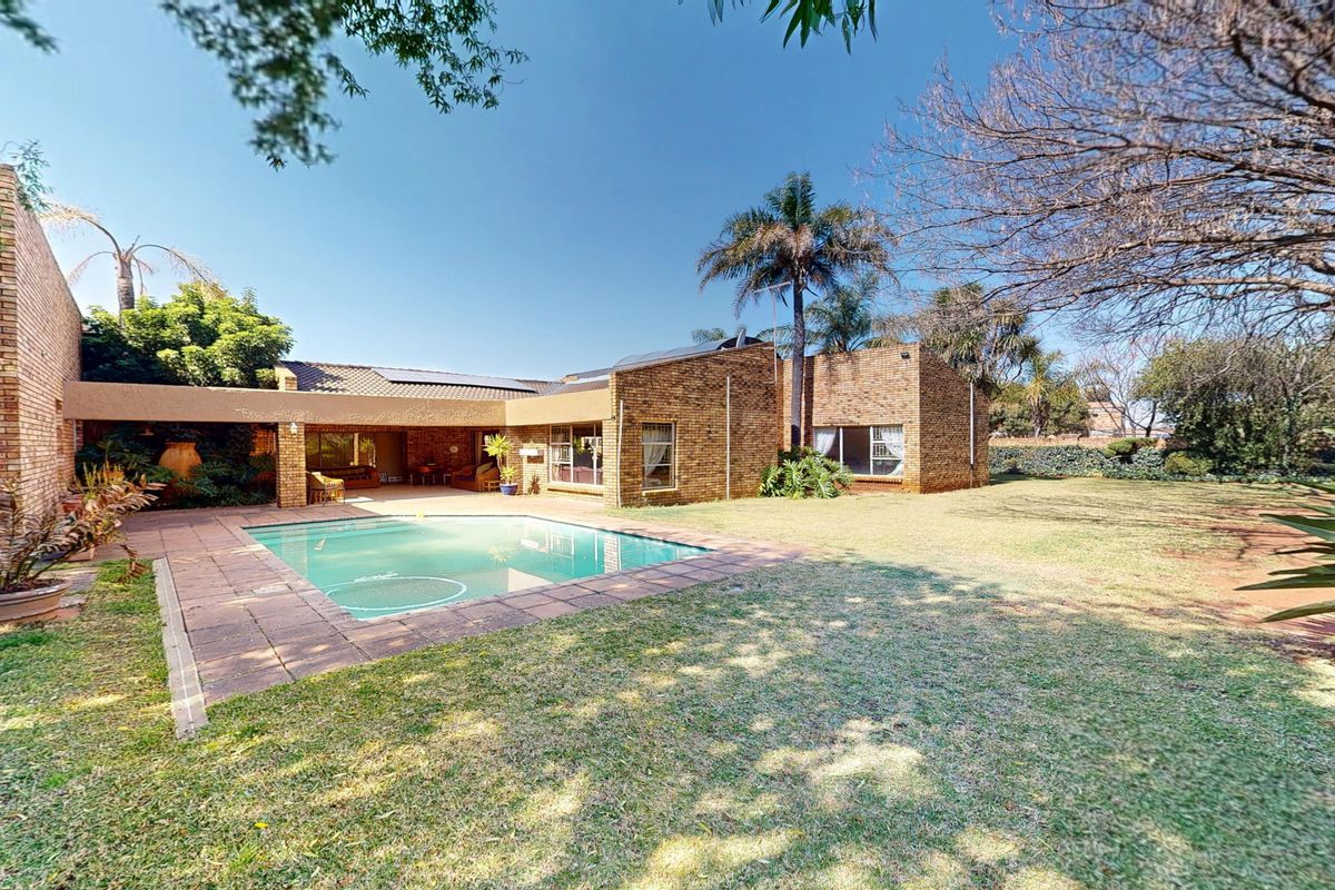 Rear view of the property featuring a brick facade, a swimming pool with paved surround, a covered patio area, and a spacious garden.