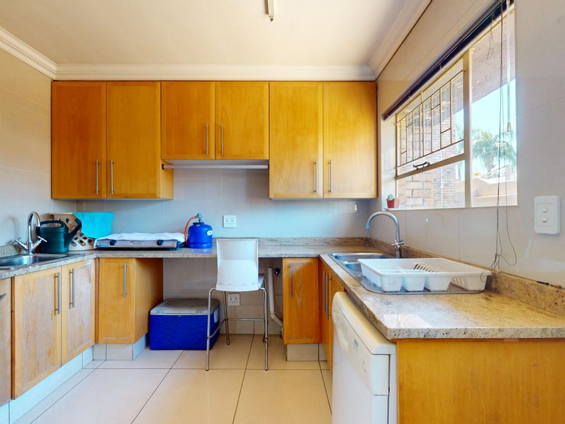 Functional kitchen featuring wooden cabinetry, granite countertops, tiled flooring, and a double stainless steel sink with natural light from the window.