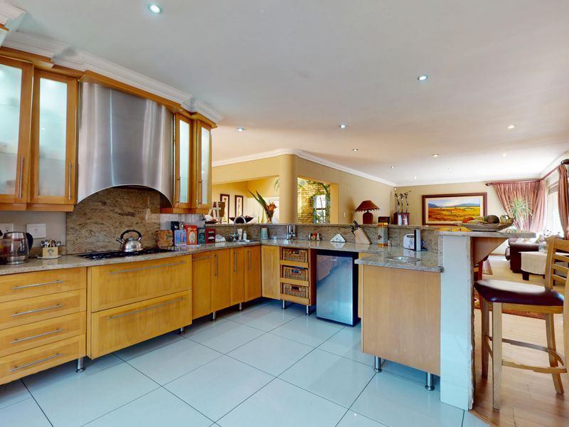 Spacious open-plan kitchen featuring light wood cabinetry, granite countertops, stainless steel appliances, and a breakfast bar, seamlessly flowing into the adjacent living area.